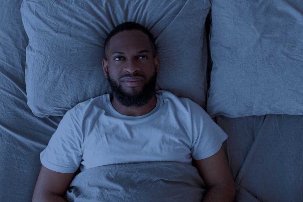 Apathy And Insomnia Concept. Above top view portrait of depressed young black man lying in bed alone and feeeling upset, thinking about problems, feeling lonely, looking up at ceiling
