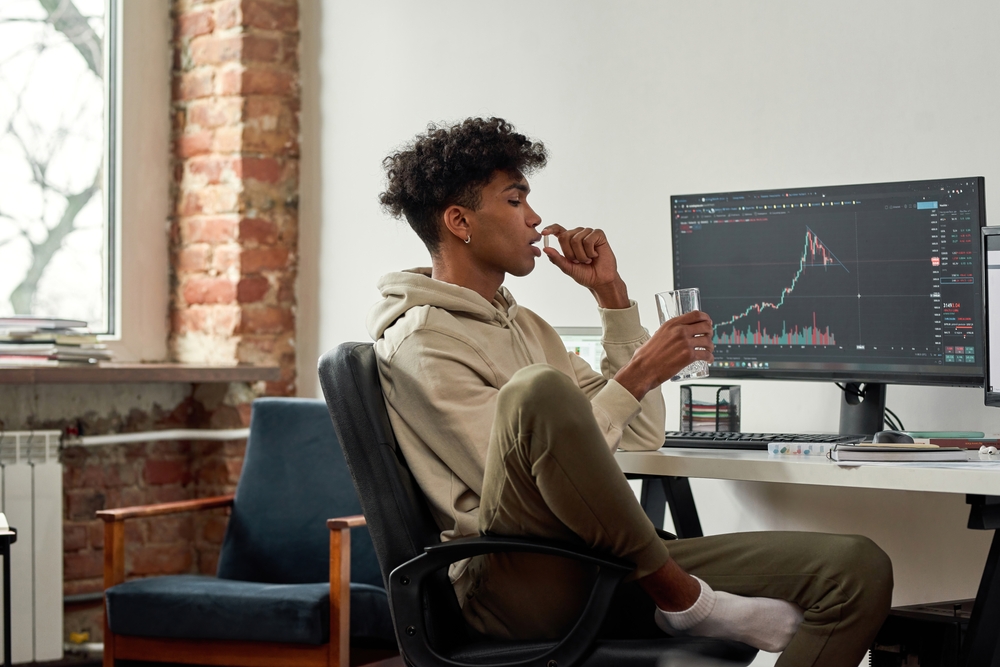 Multiethnic stock trader with glass of water taking capsule of dietary supplements for best mental work. African american trader with glass of water drinks pill while working at home modern office.