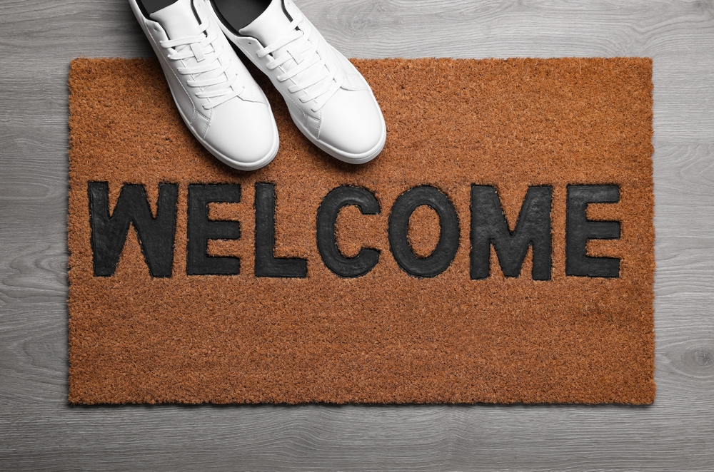 New clean mat with word WELCOME and shoes on floor, top view
