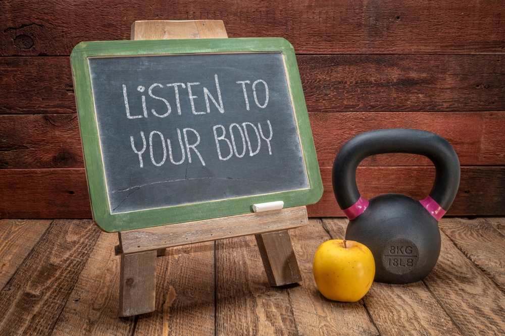 Listen to your body reminder - slate blackboard sign against weathered red painted barn wood with a kettlebell, wellbeing and fitness concept
