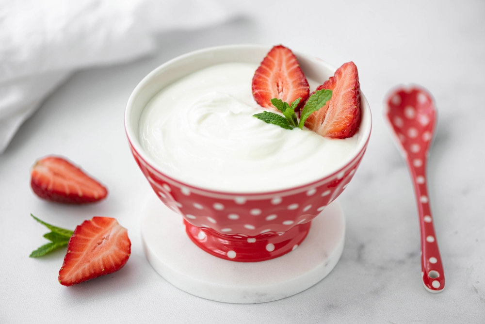 fresh homemade greek yogurt with fresh strawberries in a red bowl, close-up