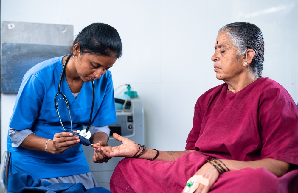 doctor or nurse checking sugar or diabetes level of hospitalised sick woman in operation gown bed - concept of health monitoring and treatment and professional occupation.
