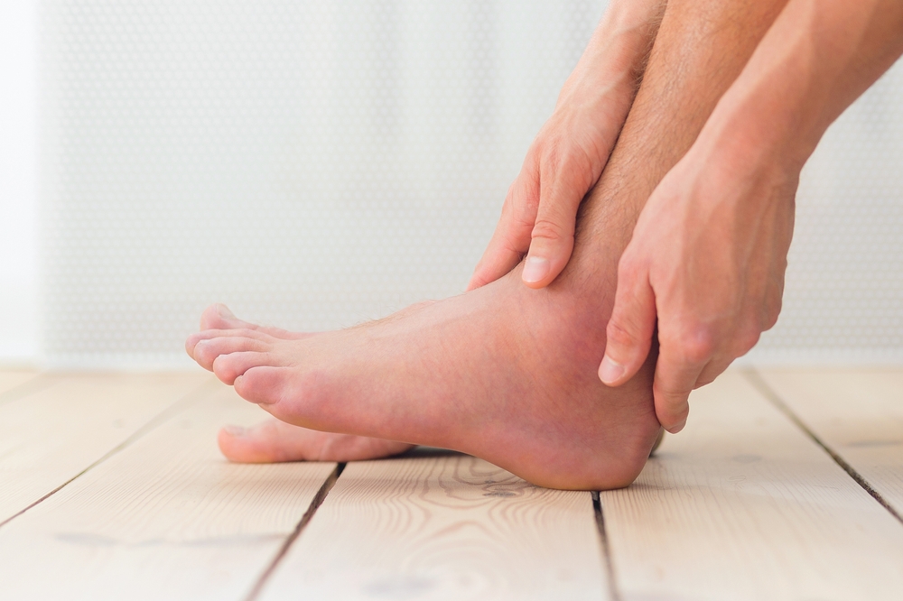Sprained and swollen ankle. Man hold his sprained ankle sitting on the sofa at home. Ankle sprain. Injury.