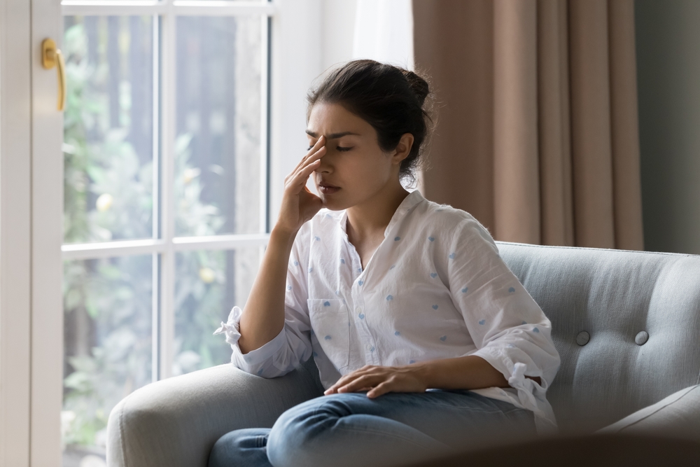 Depressed frustrated young Indian woman suffering from headache, migraine, touching face, head with closed eyes, feeling stressed, sick, tired, thinking over bad news, problems, crisis
