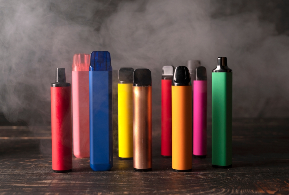 Set of colorful disposable electronic cigarettes on a dark wood background with smoke. The concept of modern smoking, vaping and nicotine.