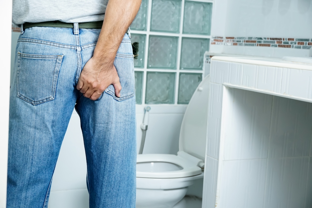 Man with diarrhea problem, Man with digestive problem touching his buttock, man with hemorrhoid problem. blurry bathroom background.