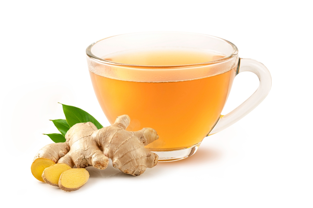 Glass cup of hot ginger tea with ginger root and slices isolated on white background.