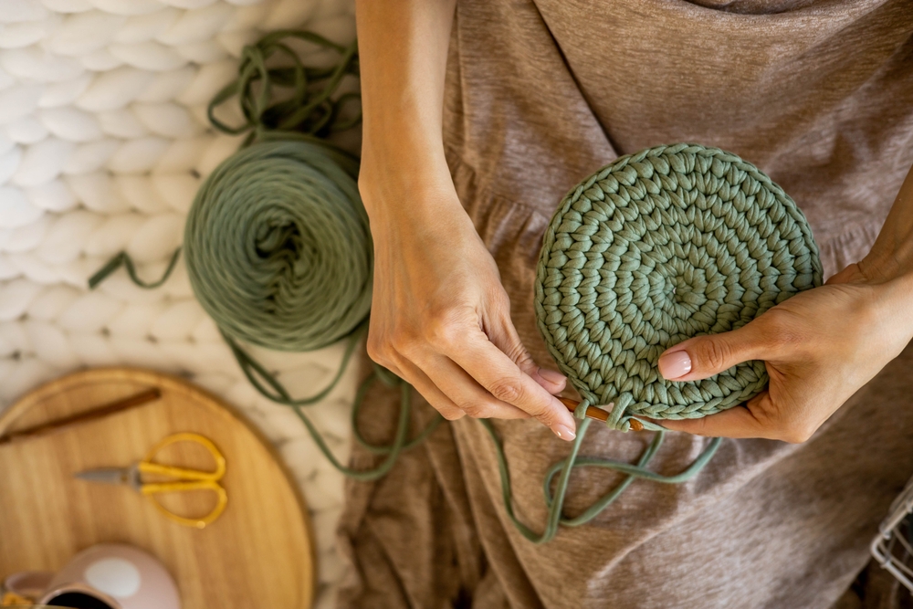Closeup female hands knitting interior decor basket use green ribbon yarn and crochet needle. Creative woman arms enjoying needlecraft hobby or art work making comfortable cotton sewing accessories