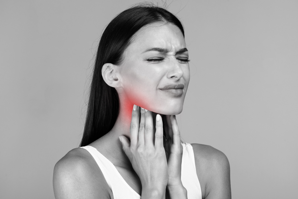 Black and white photo of young sick lady suffering from tonsillitis, pulping her lightened in red neck, experiensing acute throat pain, copy space, closeup
