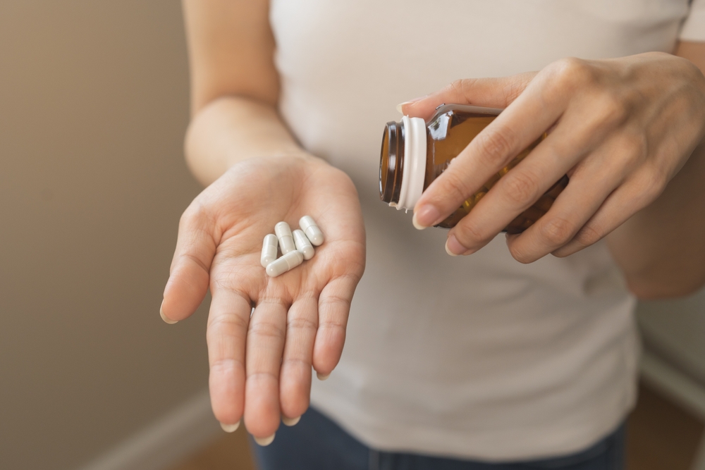 Dietary supplement or sick, asian young woman, girl hold pills, drugs medical tablet on hand pouring capsules from medication bottle, take vitamin for treatment for skin, hair at home, healthcare.