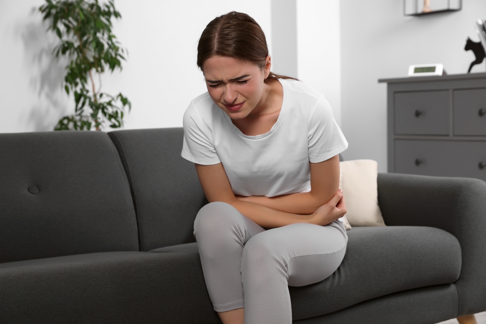 Young woman suffering from cystitis on sofa at home

