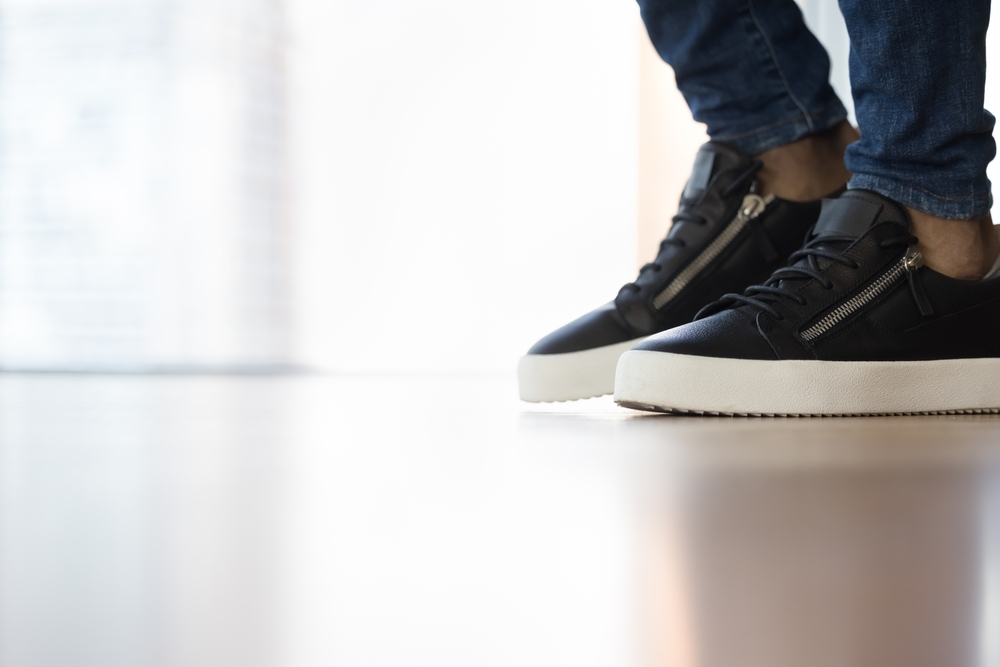 Feet in stylish sneakers of unknown African man standing or walking on clean laminate floor inside modern hotel, house or apartment, close up shot. Floor repair and installation services advertisement
