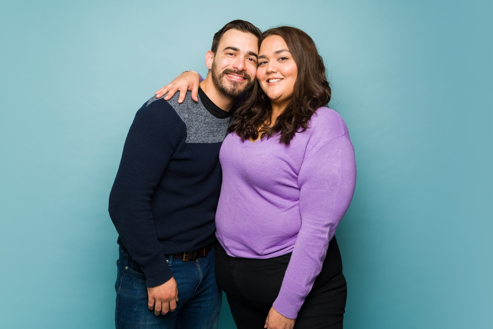 Beautiful smiling young couple dating and hugging while looking happy in front of a studio background