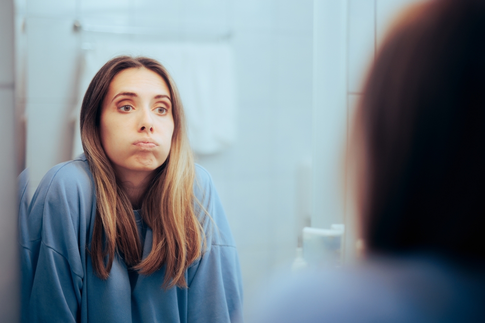 Unhappy woman Looking in the Mirror Feeling Overwhelmed. Bored millennial girl puffing being tired and insecure
