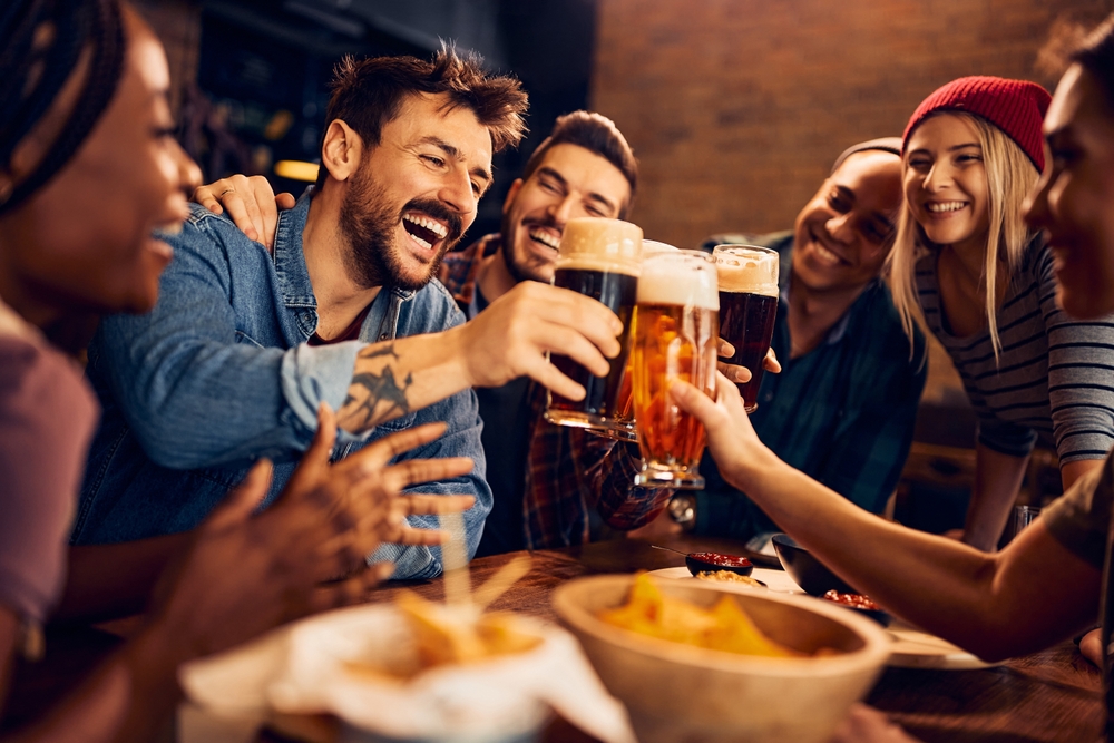 Multiracial group of happy friends having fun while toasting with beer in a bar.