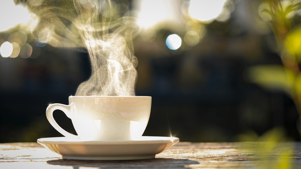 Concept Coffee Cup, Mug, hot drink, espresso, breakfast. close-up natural steam smoke of coffee from hot coffee cup on old wooden table in morning warm sunlight flare, outdoor background
