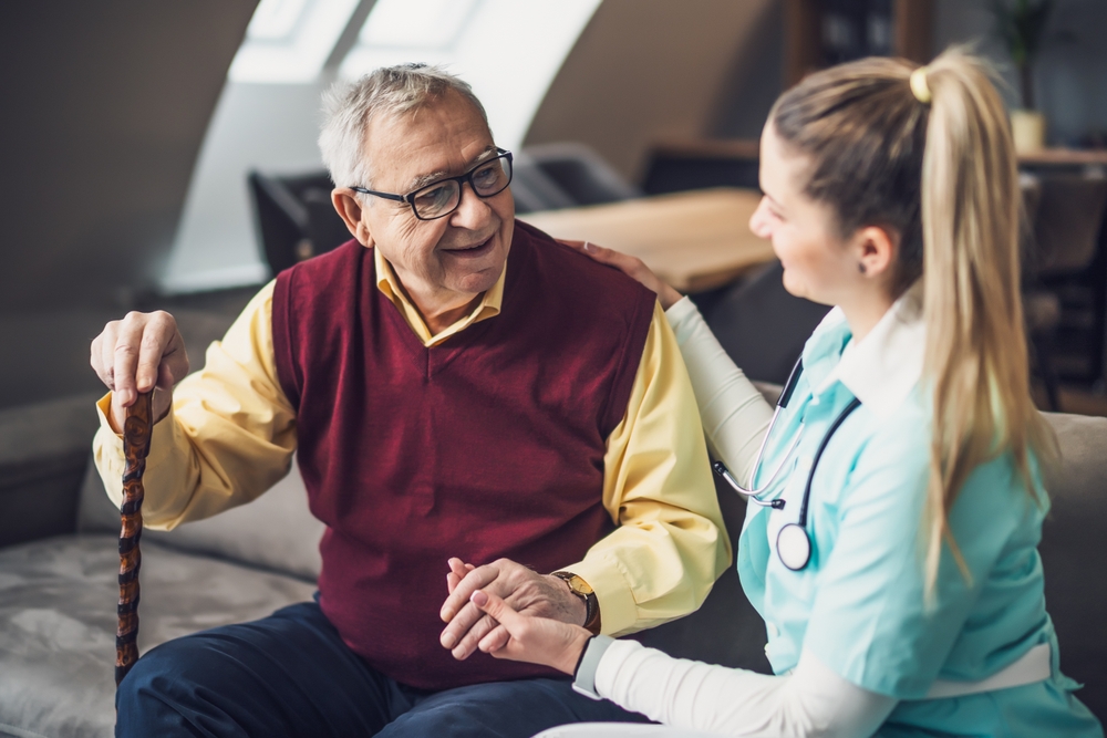 Nurse home caregiver is assisting old man at his home. Professional health support for elderly people.