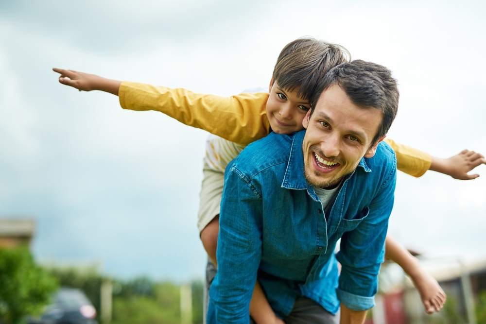 Portrait, children and a son on back of his dad outdoor in the garden to fly like an airplane while bonding together. Family, kids and a father carrying his boy child while playing a game in the yard