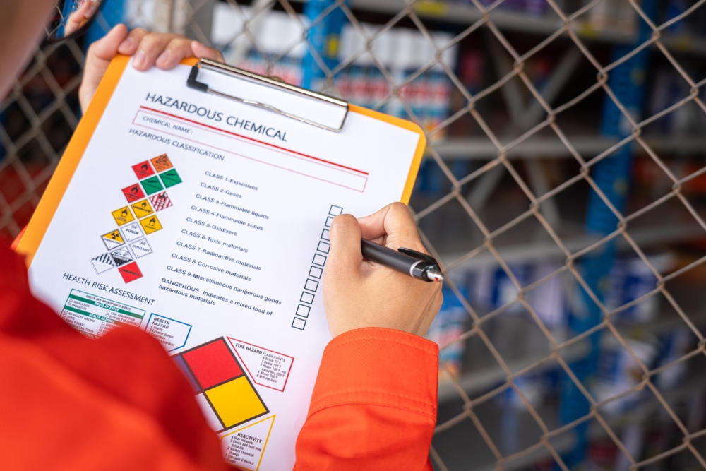 A worker is checking on the hazardous chemical material information form with background of chemical storage area at the factory place. Industrial safety working action. Selective focus.