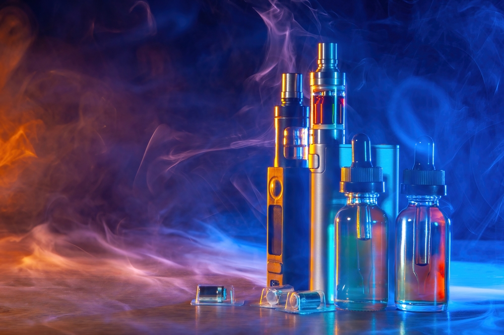 Vape devices in smoke. Electronic cigarettes on table. Small bottles of vaping oil. Vaper gadgets. Alternative to tobacco smoking. Vape cigarettes in neon light. Sale of vape gadgets concept