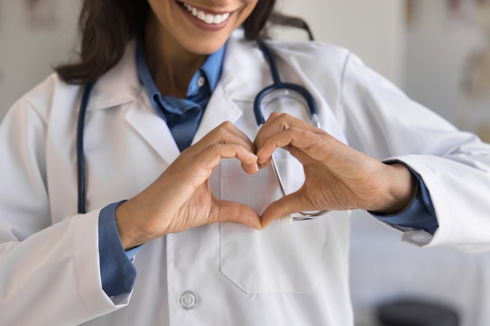 Cropped shot of young doctor woman showing hand heart, keeping romantic finger gesture at chest, expressing love, care, support for patients, early cardio disease diagnosing, checkup. Close up
