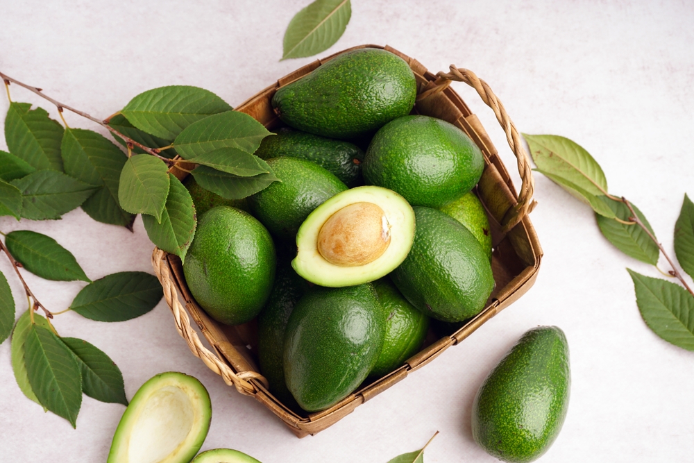 Basket with fresh ripe avocados and leaves on white background
