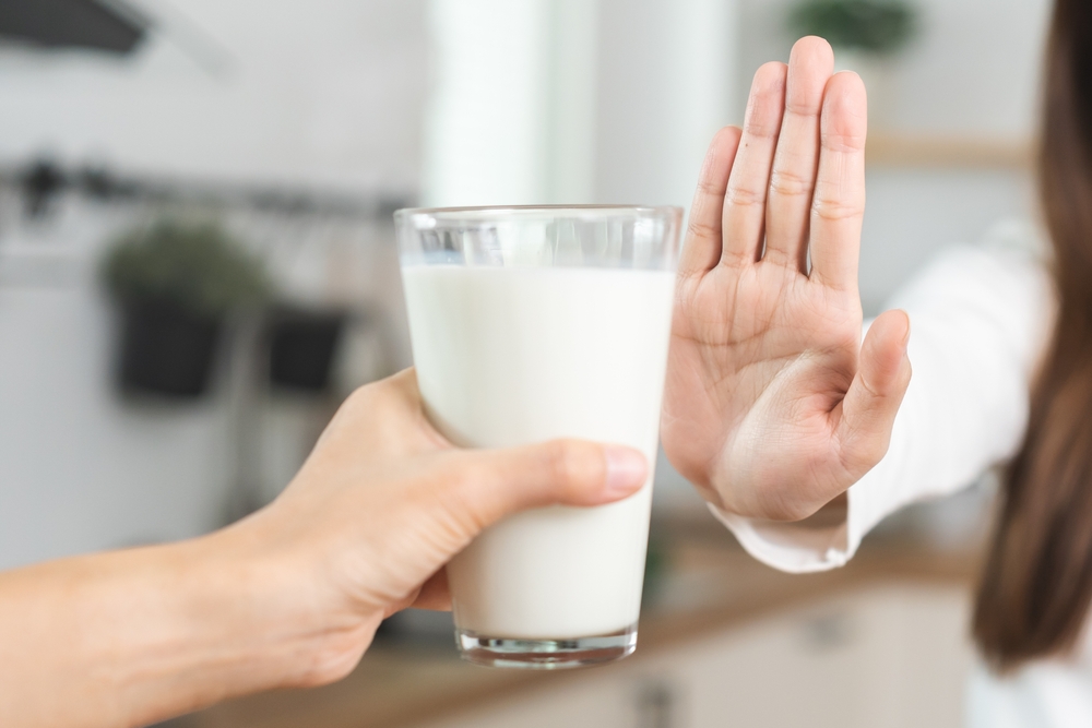 Allergy asian young woman, girl hand in deny, no or push out to avoid for drink milk at home, unhappy and bad stomach ache. Lactose intolerance and dairy food, health problem, belly suffer concept.
