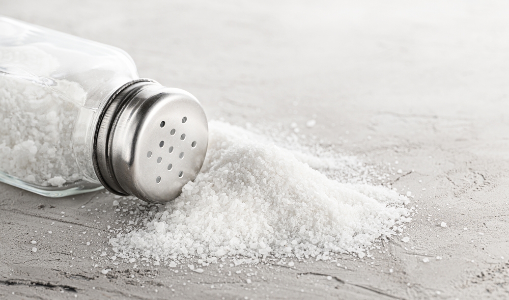 Salt shaker and pile of spilled salt on concrete stone.
