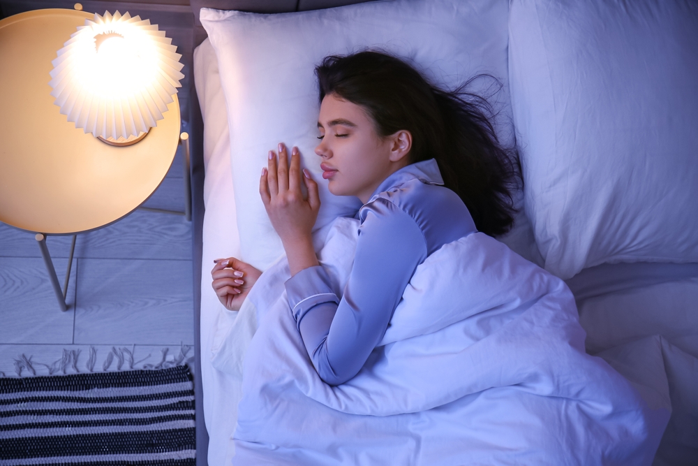 Beautiful young woman sleeping in bedroom at night, top view