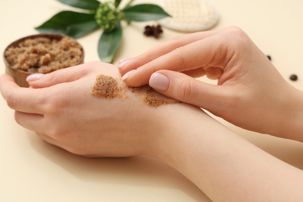 Woman applying coffee body scrub onto her hands on color background, closeup
