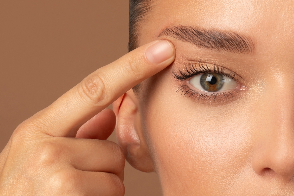 Closeup of young European woman pointing to the wrinkles on the upper eyelid, touching face. Blepharoplasty concept
