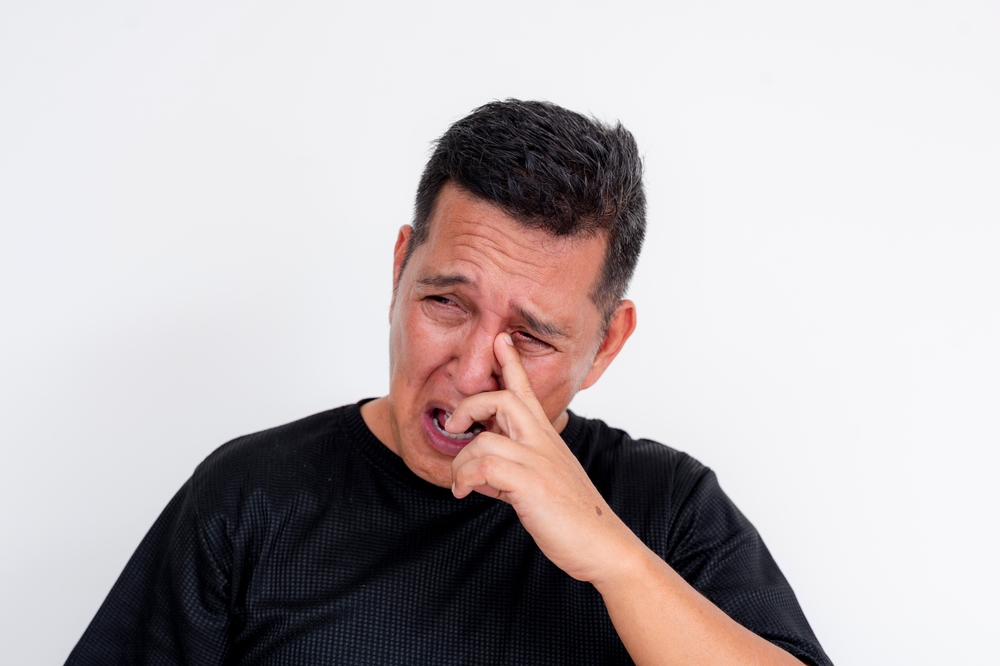A man removes Rheum or eye discharge from his tear duct. Isolated on a white background. Possible conjunctivitis, sty or other infection.
