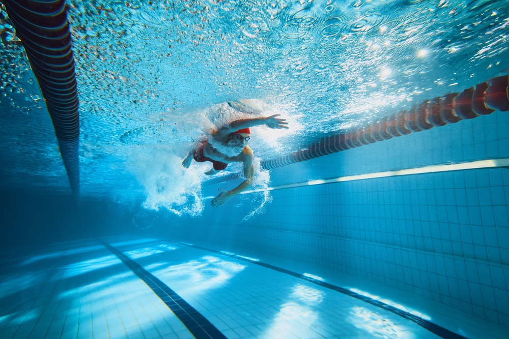 Dynamic image of young man, swimmer in motion, swimming freestyle stroke in pool, training. Concept of professional sport, health, endurance, strength, active lifestyle
