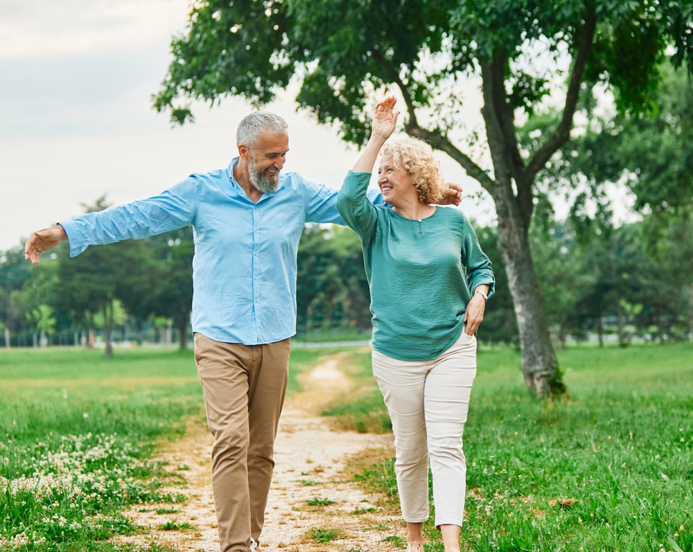 Happy active middle aged white couple having fun walking holding hands and bonding in park outdoors