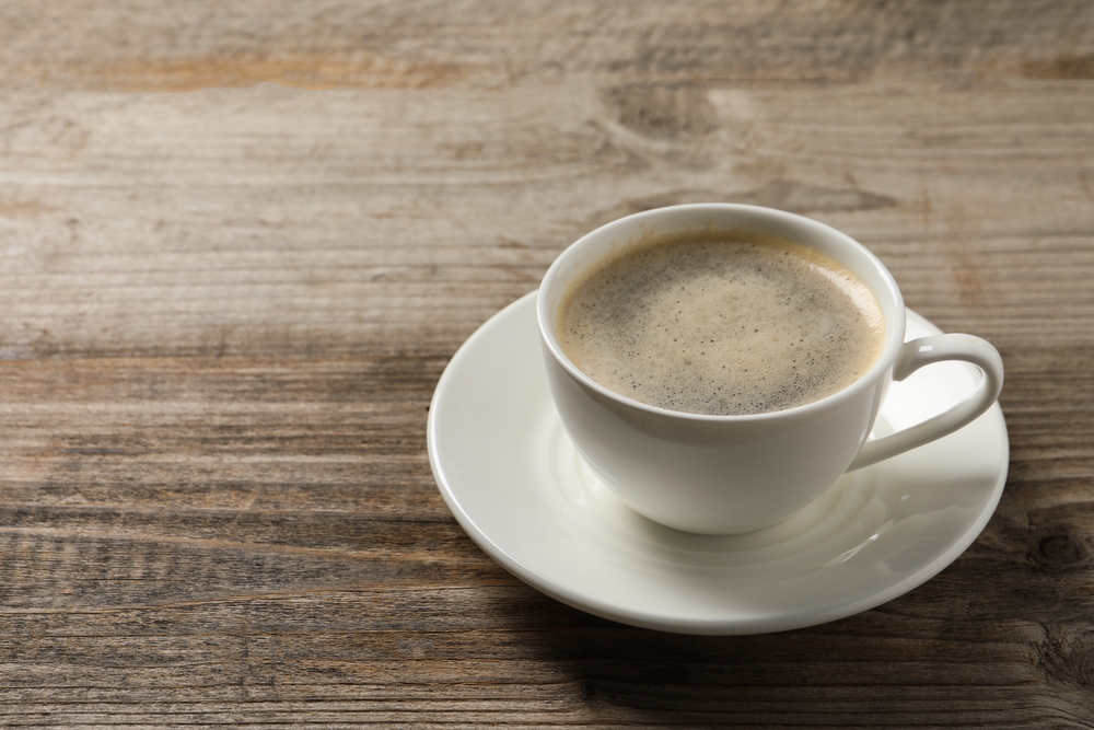 Tasty coffee in cup on wooden table, closeup. Space for text
