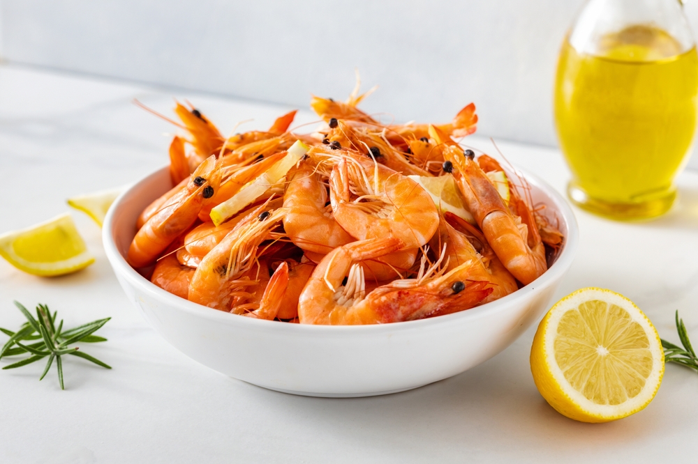 A white bowl filled with boiled shrimps garnished with lemon slices
