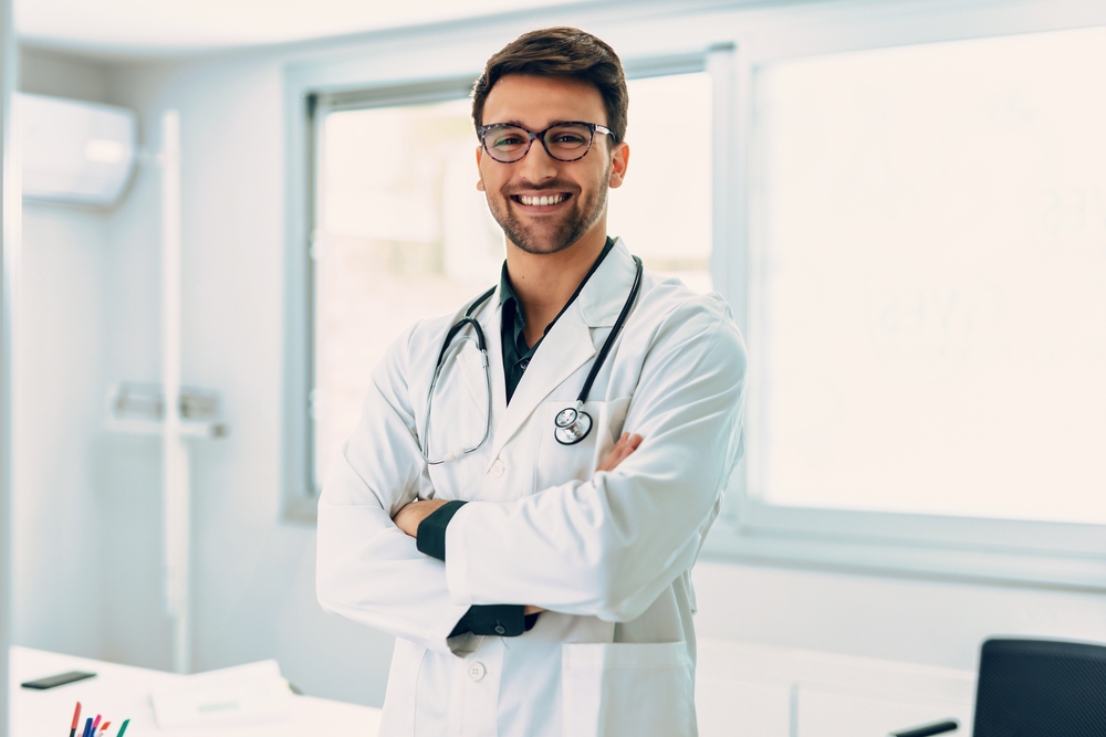 Portrait of handsome male doctor with stethoscope over neck working while looking at camera in the medical consultation.
