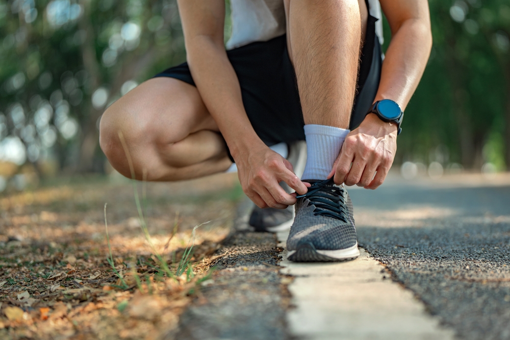 Close up - Running shoes runner man tying laces for summer run in forest park. Jogging girl exercise motivation health and fitness exercise.