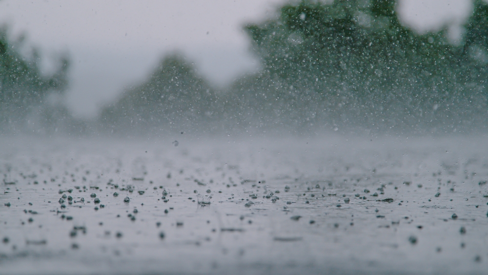 LOW ANGLE, CLOSE UP, DOF: Cinematic shot of hail falling on the asphalt during a heavy tropical rainstorm. Small pellets of ice fall on the wet concrete ground during hailstorm on a gloomy summer day.