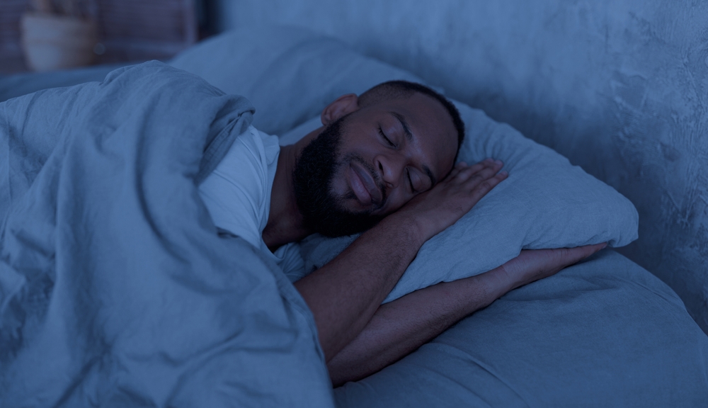 Healthy Sleeping Concept. Portrait of happy young well-slept African American man lying in bed with closed eyes, resting in bedroom on the side in the dark night, having hap