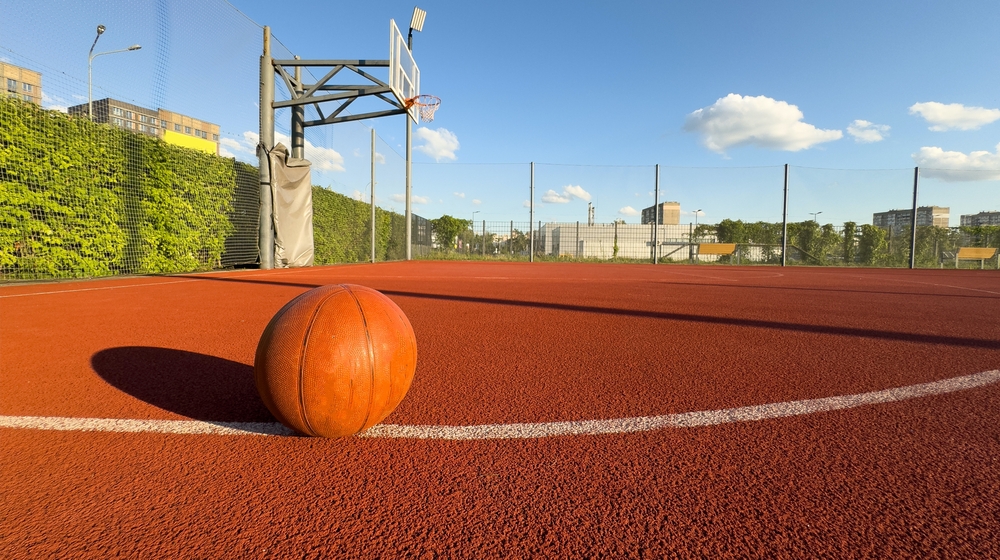 Basketball ball on the ground. Close-up ball on the red court. Basketball on the street or indoor court. Sports gear without people. Minimalism. Template, sport background