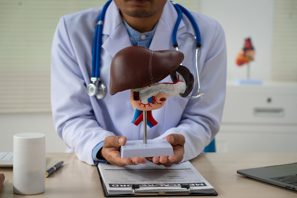 A male doctor sits at a table in a liver disease clinic, giving online advice on hepatitis A, D, E, pancreatitis, fatty liver, cirrhosis, liver cancer, and pancreatic cancer.
