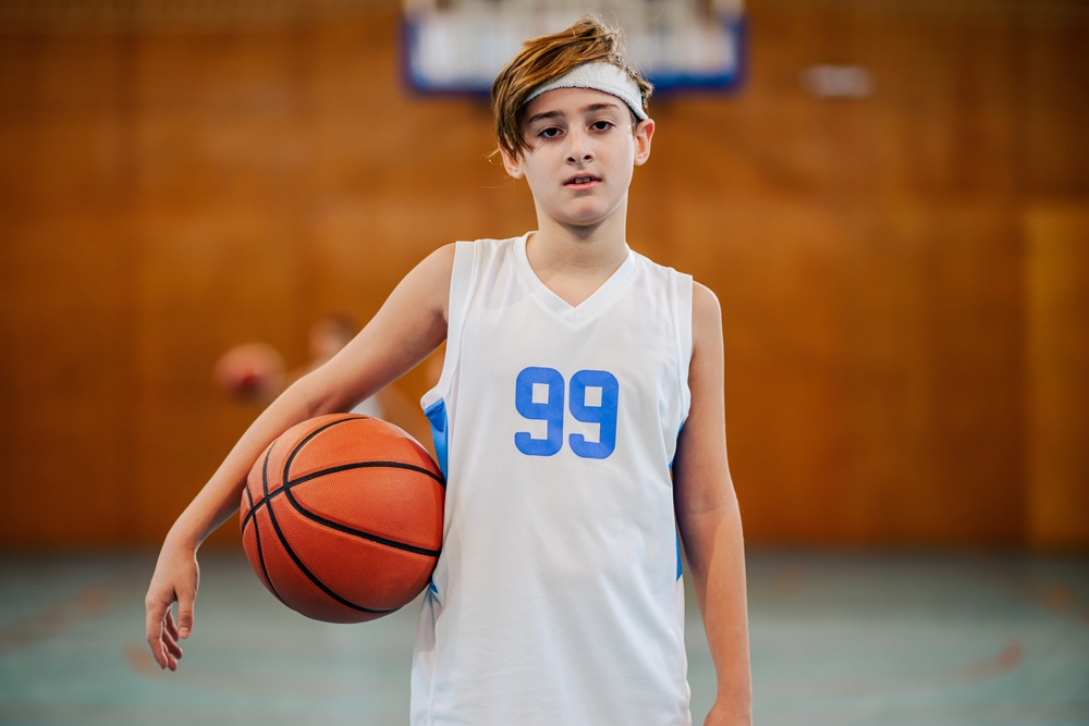 Confident kid athlete in jersey number 99 poses with a basketball, exhibiting sporting spirit and enthusiasm