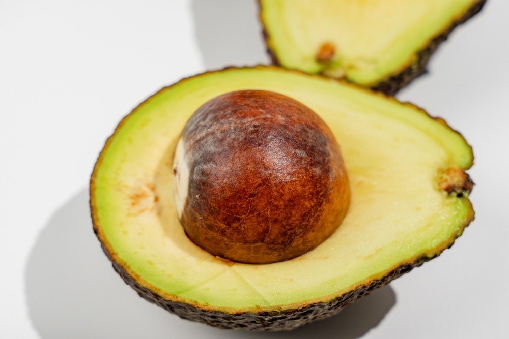 Avocado with brown pit. The avocado is cut in half and the pit is visible inside.
