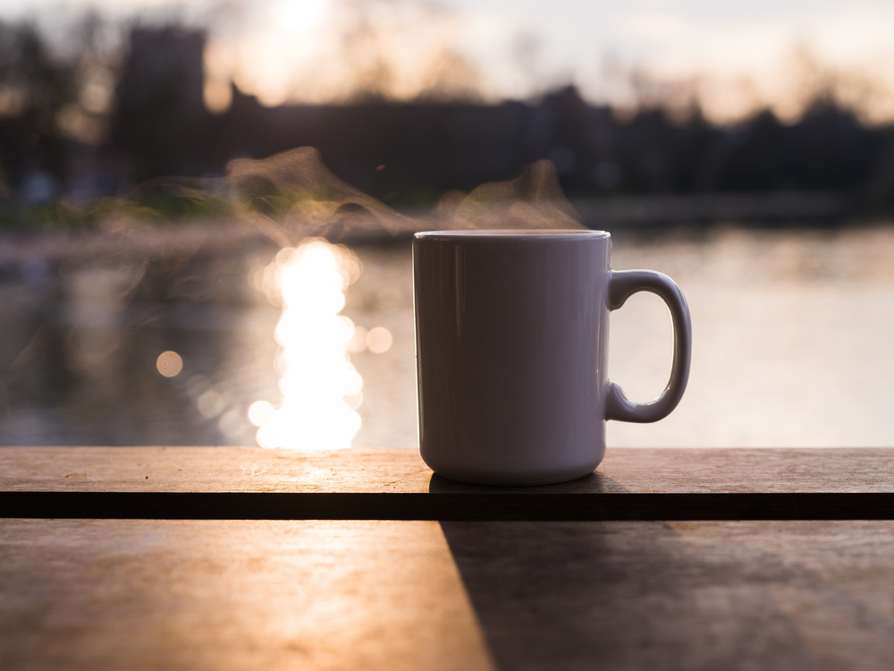 Steam rising from a mug with a hot beverage by a pond at sunset in the winter
