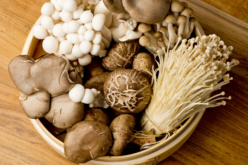 Mushrooms. Fresh Organic, enoki, shiitaki, hen of the woods, baby portabello, button mushrooms in wooden woven basket at a restaurant. Variety of Mushrooms in a basket, closeup and shot overhead.
