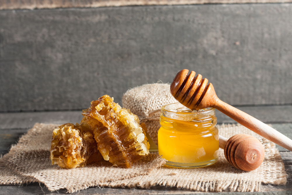 Honey dripping from a wooden honey dipper in a jar on wooden grey rustic background