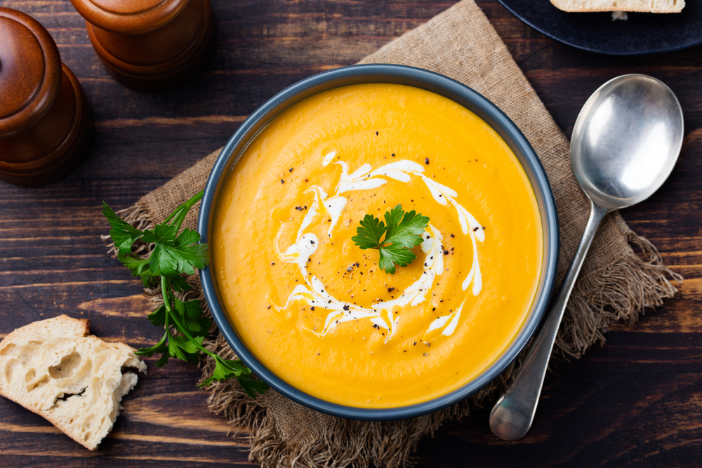 Pumpkin and carrot soup, tadka with cream and parsley on dark wooden background. Top view.