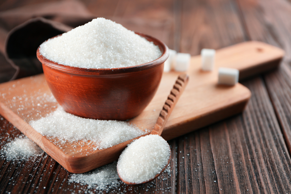 Bowl and spoon full of sugar on wooden background