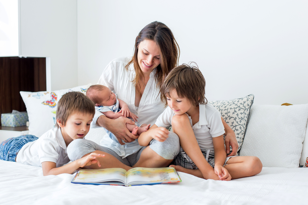 Young mother, read a book to her three children, boys, in the bedroom, mothers day concept